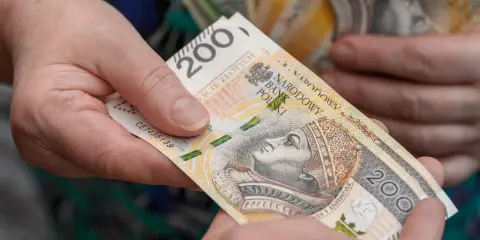 Dwie dłonie przekazują sobie banknot 200 zł. Czy opieka nad dzieckiem niepełnosprawnym wlicza się do emerytury?