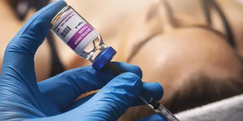 Mano con guanto blu che aspira botulino da fiala. Si valuta il botox mento effetti collaterali.