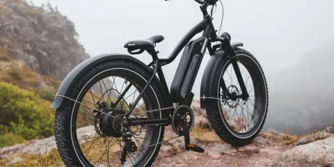 Czarny rower elektryczny z grubymi oponami, idealny dla otyłych, stoi na skalistym podłożu w mglistym krajobrazie.