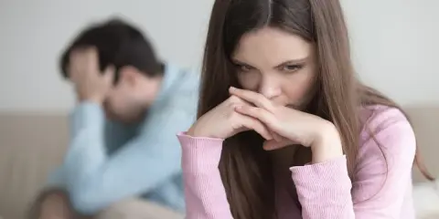 Zmartwiona kobieta z dłońmi przy ustach, obok mężczyzna z ręką na głowie. W tle widać kanapę. Obraz symbolizuje **relationship ocd**.