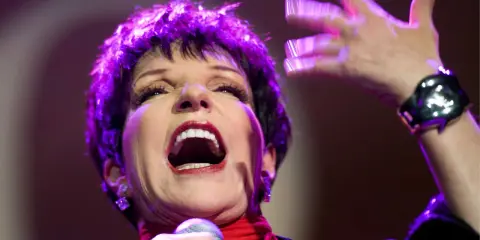 Liza Minnelli, en ikonisk artist, sjunger med passion på scenen, hennes ansikte upplyst av lila ljus.