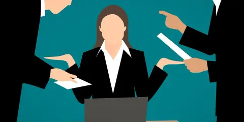 Kobieta przy biurku z laptopem, otoczona przez dwóch mężczyzn, którzy wskazują na dokumenty. Wygląda na to, że jest to sytuacja z zażaleniem po angielsku.