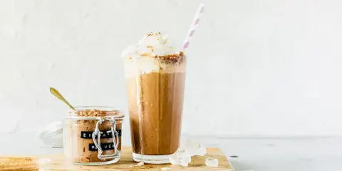 Eiskaffee mit gekochtem Kaffee, zubereitet im Thermomix, gekrönt mit Sahne. Daneben ein Glas mit Eiskaffee-Pulver.