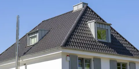 Dach kopertowy konstrukcja z ciemnej dachówki, z lukarnami i kominem.