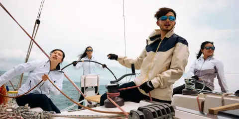 Kto to jest skipper? Młody mężczyzna w okularach przeciwsłonecznych kieruje jachtem, podczas gdy jego załoga pracuje przy linach.