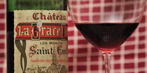 Ein Glas Rotwein neben einer Flasche Château La Grace Dieu, ein Saint-Émilion Grand Cru.