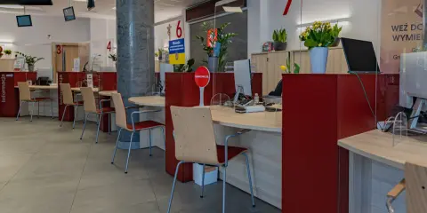 Puste biurka z krzesłami w urzędzie, gdzie przestrzegana jest proksemika. Widać numery stanowisk i tabliczki informacyjne.
