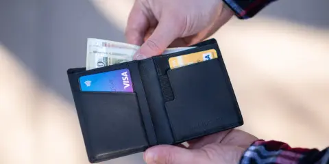 Dłonie wkładają pieniądze i kartę Visa do czarnego portfela.
