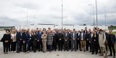 Grupa osób przed bateryjnymi magazynami energii, symbolizującymi rozwój polskiego stowarzyszenia magazynowania energii.
