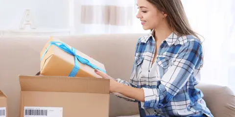 Uśmiechnięta kobieta pakuje prezent. To część wysyłki na Litwę, starannie przygotowana do podróży.