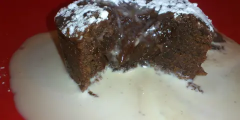 Un fondant au chocolat dégoulinant, saupoudré de sucre glace, servi dans une sauce crémeuse sur une assiette rouge.