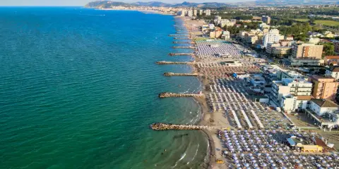 Vista aerea della costa adriatica, con la spiaggia affollata di ombrelloni e stabilimenti balneari, che si estende fino a Cattolica e Misano.