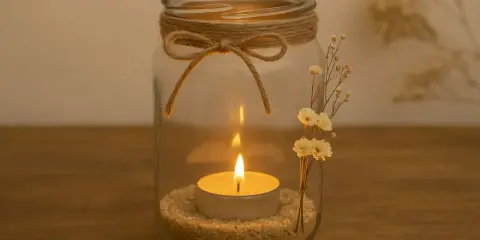 Ein Glas mit Sand, Teelicht und getrockneten Blumen. Mit Juteband und Schleife verziert – so einfach lassen sich schöne Teelichthalter basteln.