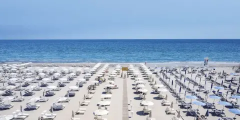 File di ombrelloni bianchi e lettini ordinati sui **stabilimenti balneari Cervia**, con il mare azzurro sullo sfondo.