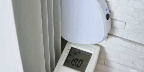 Schéma branchement thermostat chauffage électrique : un boîtier blanc "heatzy" et une télécommande affichant 19.0°C, près d'un radiateur.