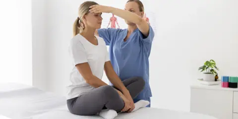 Fizjoterapeuta wykonuje masaż sportowy głowy u pacjentki siedzącej na kozetce.