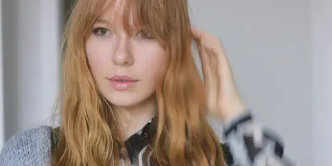 Ein junges Mädchen mit langen, welligen Haaren und Pony, das sich die Haare stylt.