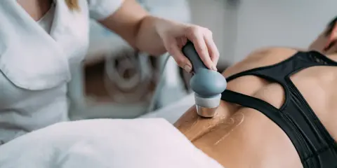 Rehabilitacja ultradźwięki na czym polega? Fizjoterapeuta wykonuje zabieg ultradźwiękami na plecach pacjentki, co pomaga w leczeniu bólu i regeneracji tkanek.