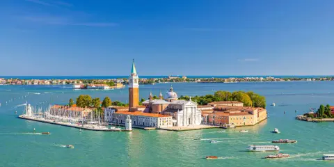 Vue aérienne de Venise, le campanile San Giorgio Maggiore se dresse fièrement sur son île, entouré d'eaux turquoise et de voiliers.