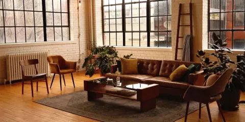 Przytulny salon w stylu loft aranżacje. Brązowa skórzana kanapa, drewniane meble i duże okna tworzą ciepłą atmosferę.