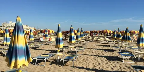 Ombrelloni a righe blu e gialle e lettini vuoti sulla spiaggia di Rivazzurra, in attesa dei bagnanti.