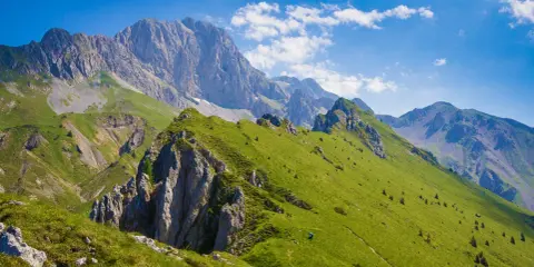 Prati verdi e sentieri invitano a **passeggiate facili** in Val Seriana, con maestose cime sullo sfondo sotto un cielo azzurro.