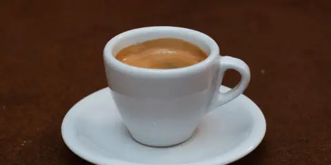 Ein kleiner weißer Becher mit cremigem, doppeltem Espresso, italienisch zubereitet, steht auf einer Untertasse.