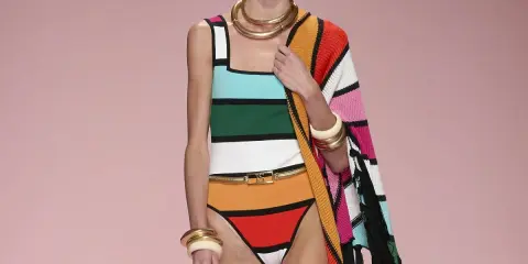 Modella con costume a righe colorate e cappello nero. Un'abbronzatura a strisce perfetta per l'estate, completata da gioielli dorati e un coprispalle a fantasia.