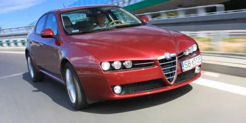 Czerwone Alfa Romeo 159 1.9 JTD pędzi po autostradzie.