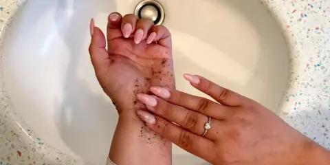 Manos con uñas largas y rosadas, cubiertas de gránulos oscuros. Parece un autobronceador mal aplicado que se está intentando lavar.