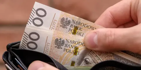 Dłoń wkłada do portfela banknoty 100 zł. Czy to na bieżące wydatki, czy może na 13. emeryturę?