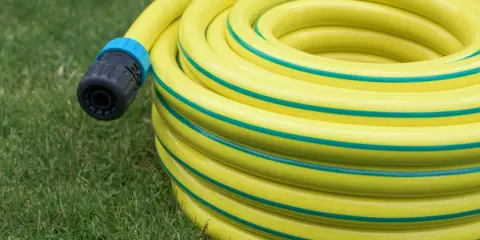 Un tuyau d'arrosage jaune enroulé sur l'herbe, avec un connecteur noir et bleu. Le diamètre du tuyau d'arrosage est visible dans son enroulement.
