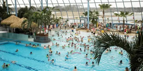 Tłum ludzi korzysta z basenów w największym aquaparku w Polsce. Palmy i tropikalne chatki tworzą wakacyjny klimat.