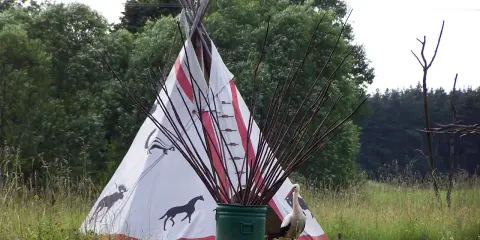 Wioska indiańska na Mazurach z tipi ozdobionym zwierzętami, bocianem i łukami.