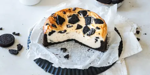 Ein cremiger Oreo Kuchen mit einem dunklen Keksboden, dekoriert mit ganzen und zerbrochenen Oreos.