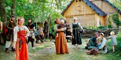 En grupp människor i vikingakläder samlas framför ett trädhus i vikingabyn Storholmen.