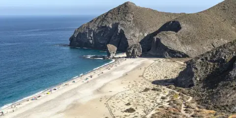 Sonnige Playa de los Muertos mit türkisfarbenem Meer, Felsen und vielen Sonnenanbetern.