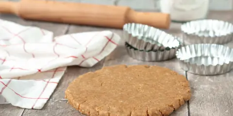Pâte sablée prête pour la cuisson au four à chaleur tournante. Rouleau à pâtisserie, moules et torchon à proximité.