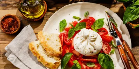 Burrata z pomidorami, bazylią i pieczywem na talerzu.
