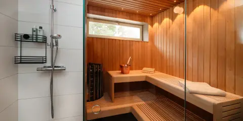 En liten bastu i badrummet, med träpaneler, bänkar och en dusch.