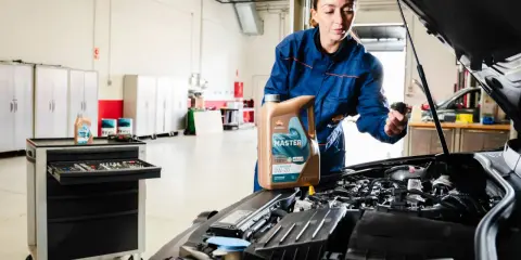 Mecánica muestra cómo cambiar el aceite del coche, sosteniendo una botella de aceite Repsol Master.