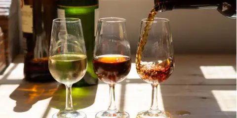 Drei Gläser mit Sherry, die die Vielfalt der sherry Herkunft zeigen. Ein helles, ein dunkles und ein drittes, das gerade eingeschenkt wird.