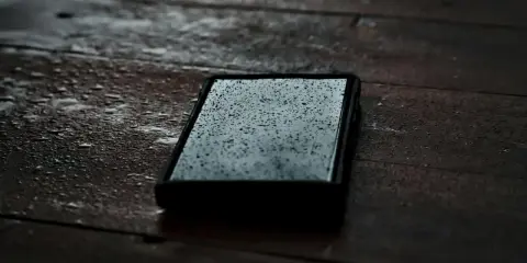 Telefon leży na mokrym drewnianym stole, pokryty kropelkami deszczu. Jego obudowa zapewnia ochronę ipx4 wodoszczelność.