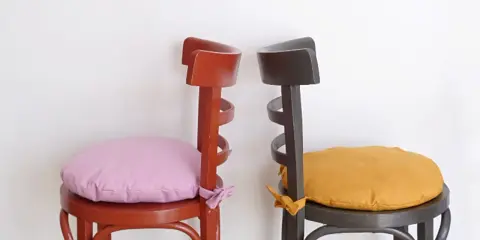 Dos sillas de madera pintadas, una roja con cojín lila y otra gris con cojín ocre. ¡Ideas para pintar sillas de madera!