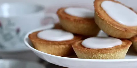 Små, gyllene mazariner med vit glasyr på ett tårtfat. Perfekt till fikat, här är ett enkelt mazariner recept.