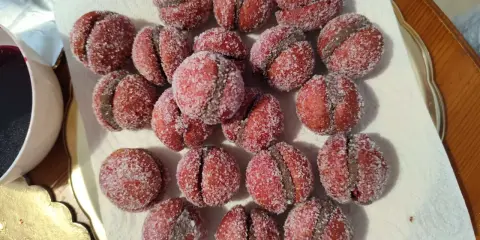 Dolci castagnole romagnole, due semisfere rosse unite da una crema scura e ricoperte di zucchero.