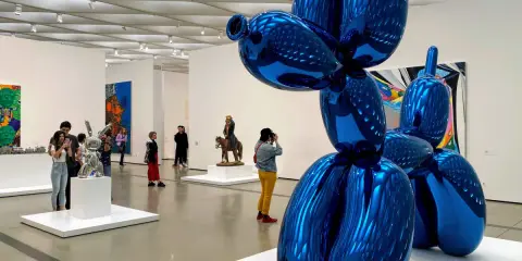 Visitors admire a giant blue balloon dog sculpture in a modern art gallery, a highlight among the top art galleries in the world.