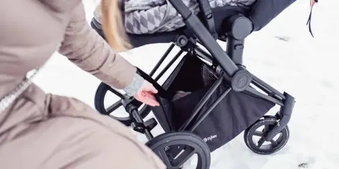 Kobieta wkłada coś do kosza wózka Cybex Priam. Waga wózka jest niewielka, co ułatwia manewrowanie w śniegu.