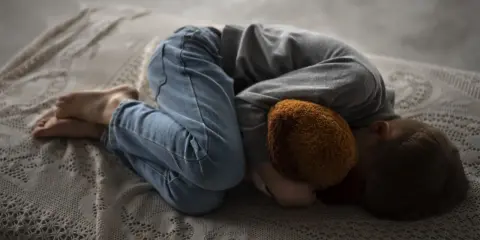 Un niño abraza un peluche, acurrucado en una cama. Una imagen que evoca la necesidad de saber como explicar la muerte a un niño.