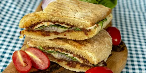 Pyszne panini z kurczakiem, suszonymi pomidorami i serem, podane z pomidorkami koktajlowymi i sałatą.